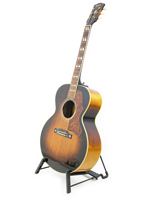 A 1952 Gibson J-185 guitar elegantly positioned on a stand with a white background.