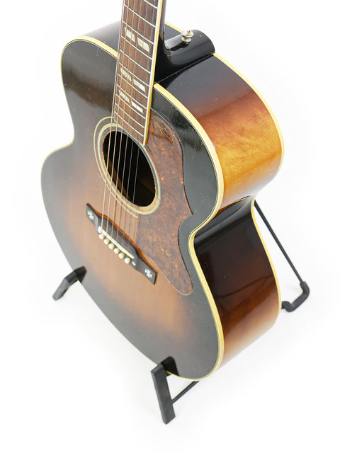 A 1952 Vintage Gibson J-185 guitar displayed on a stand, set against a simple white background for emphasis.