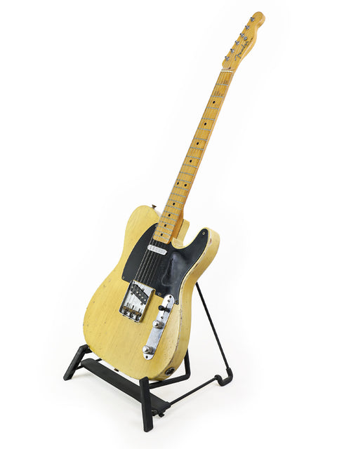 A 1954 Fender Telecaster 'Blackguard' guitar on a stand, showcasing its vintage charm against a simple white backdrop.