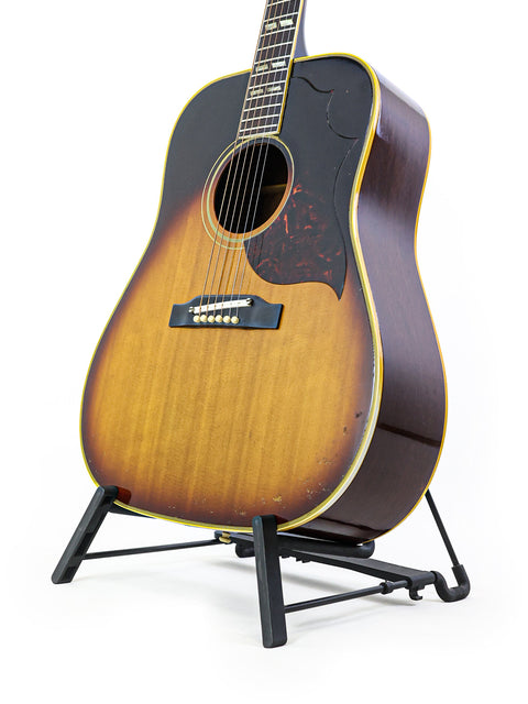 A 1964 Gibson Southern Jumbo guitar elegantly positioned on a stand with a pristine white backdrop.