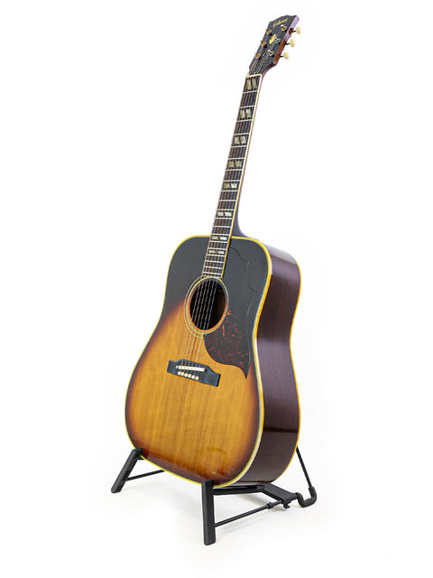 A 1964 Gibson Southern Jumbo guitar elegantly positioned on a stand with a white backdrop.