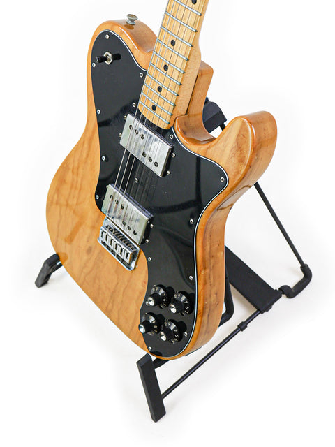 A 1973 Fender Telecaster Deluxe guitar with a wooden body, elegantly displayed on a sleek black stand.