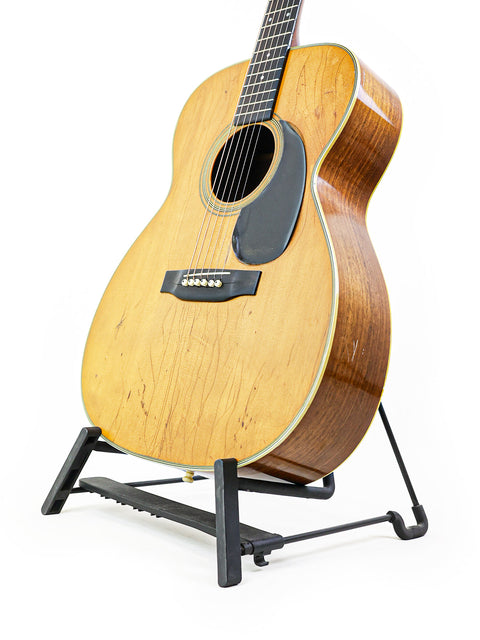 A 1974 Martin 000-28 guitar resting on a stand, set against a stark white background.