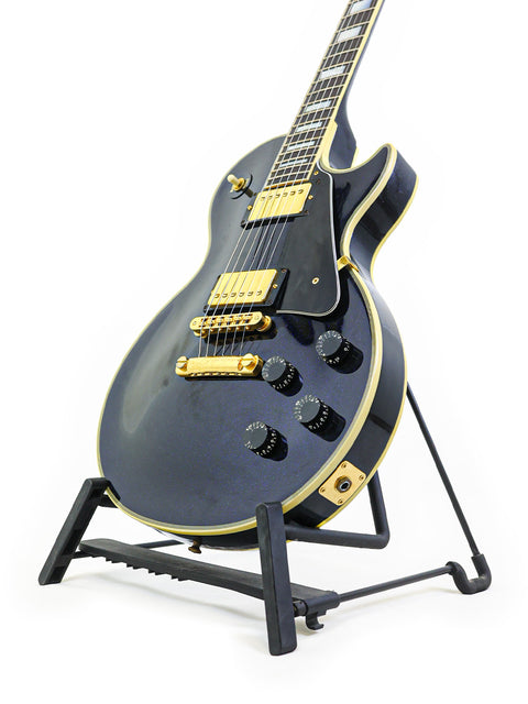 A 1991 black electric guitar, the Gibson Custom Shop Les Paul Custom, positioned on a stand for display.