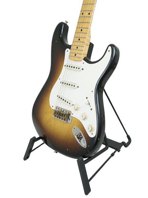 A Fender '57 Stratocaster guitar on a stand, highlighted against a black backdrop. Masterbuilt by Kyle McMillin, USA 2022