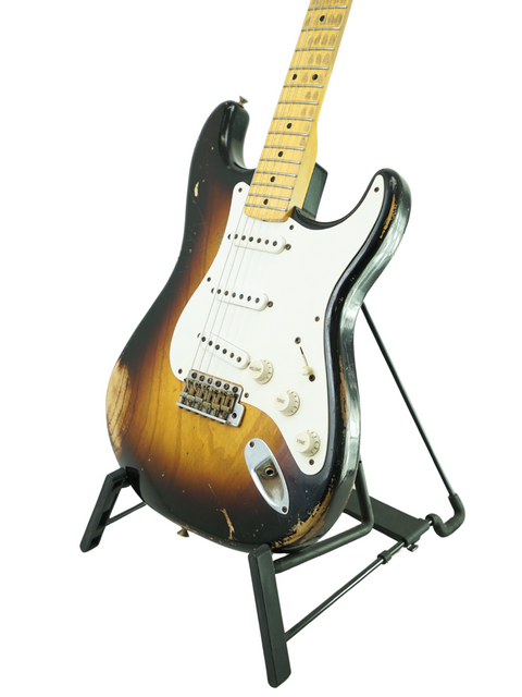 A Fender Custom Shop '54 Stratocaster Relic guitar stands out on a stand, framed by a deep black background.