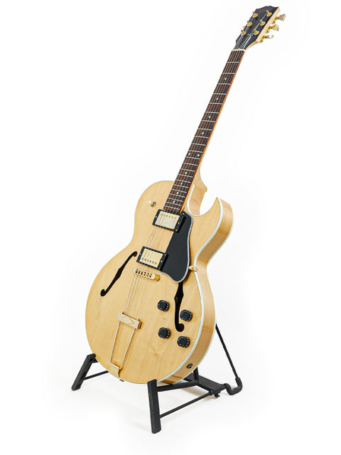 A Gibson ES-135 guitar from 2002 displayed on a stand, set against a bright white backdrop.
