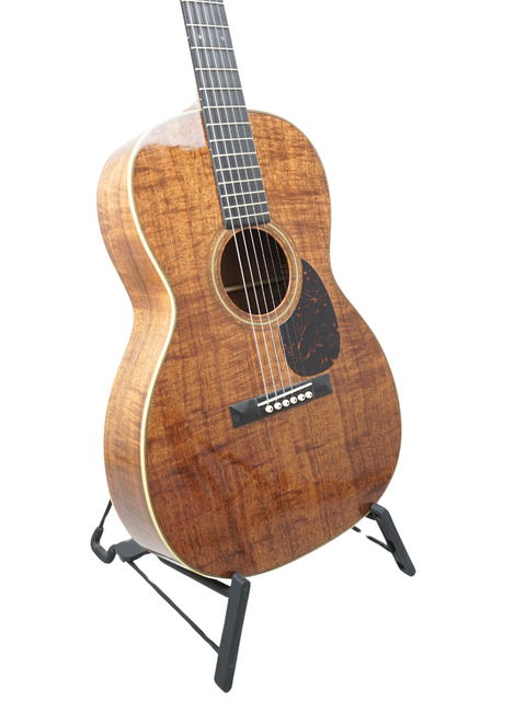A Martin 000-28K guitar with a wooden body rests on a sleek black stand, showcasing its elegant craftsmanship.