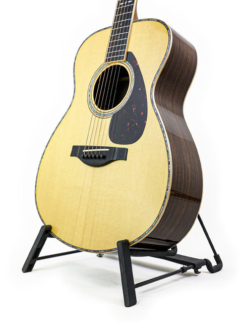 A Yamaha LS36 ARE guitar resting on a stand, with a simple white background emphasizing its elegant features.