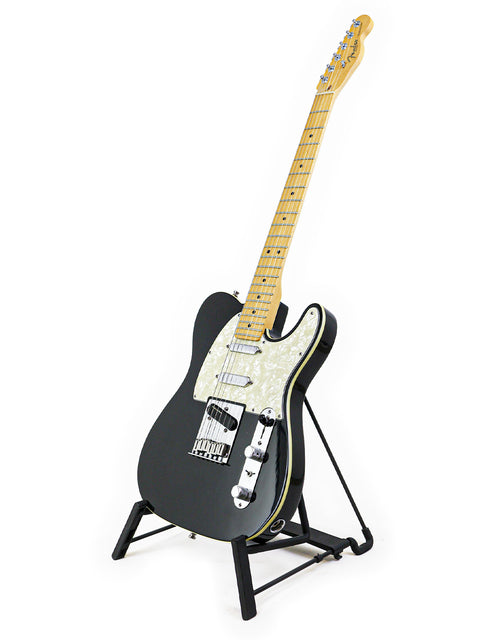 A black 1999 Fender Tele Plus V2 guitar elegantly positioned on a stand with a stark white backdrop.