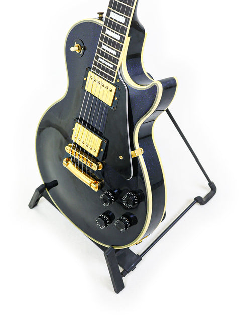 A black electric guitar on a stand, featuring the 1991 Gibson Custom Shop Les Paul Custom model.