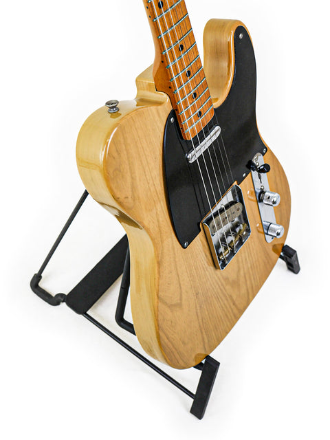 A classic black-bodied Fender AVRI ‘52 Telecaster guitar displayed on a stand, showcasing its vintage charm.