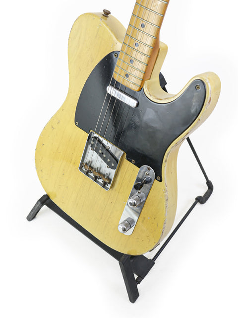 A classic yellow Fender Telecaster 'Blackguard' from 1954, resting on a stand, showcasing its vintage charm.