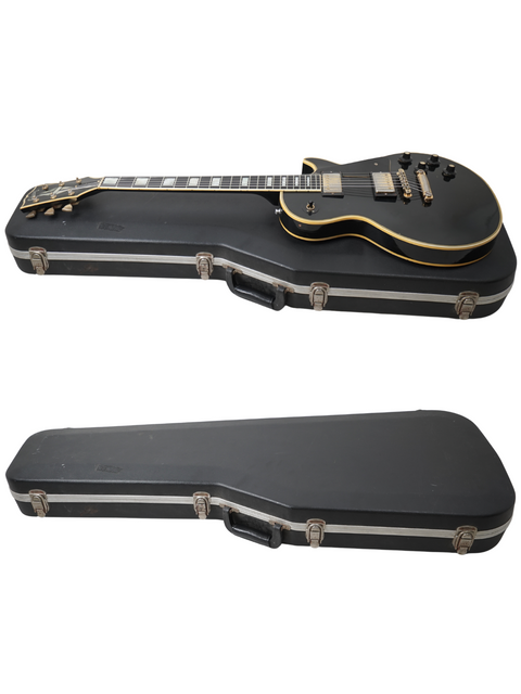 A pair of black electric guitars, featuring a 1973 Gibson Les Paul Custom, resting in cases against a white backdrop.