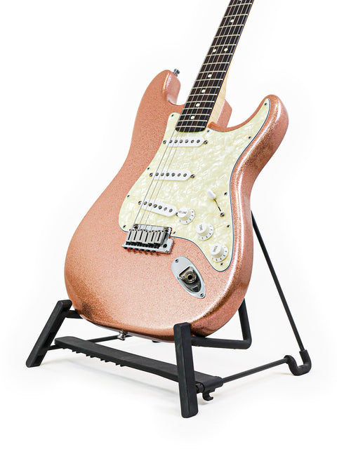 A pink 1994 Fender Custom Shop Stratocaster guitar on a stand with a black base, representing timeless musical artistry.