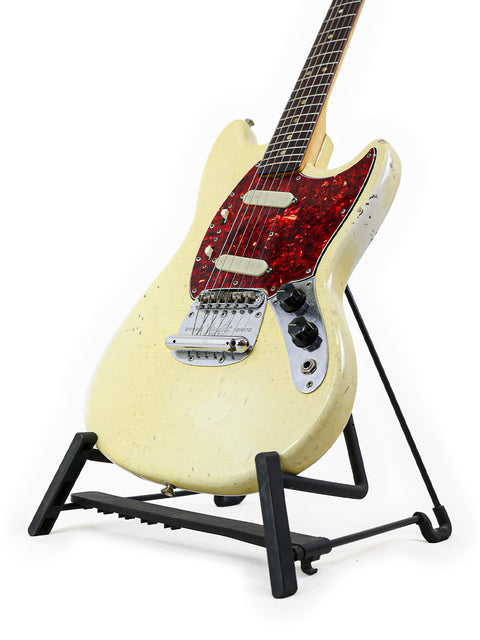 A pristine white 1967 Fender Mustang guitar on a black stand, capturing the essence of vintage rock and roll style.