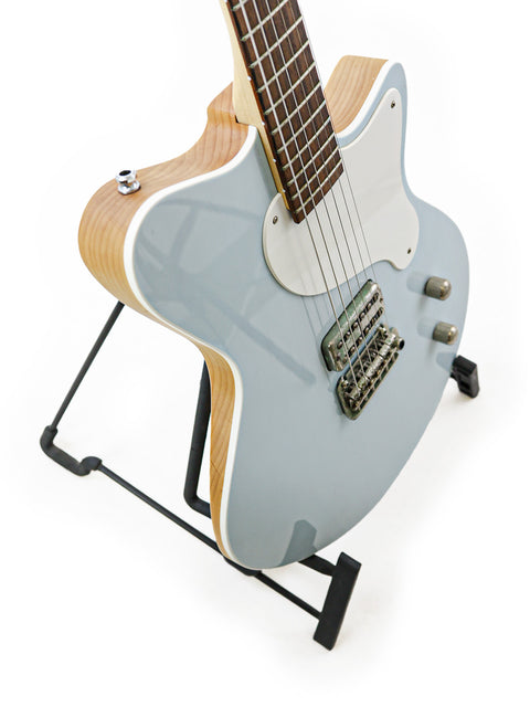 A striking blue Koll Troubadour guitar displayed on a stand, set against a minimalist white backdrop for a modern look.