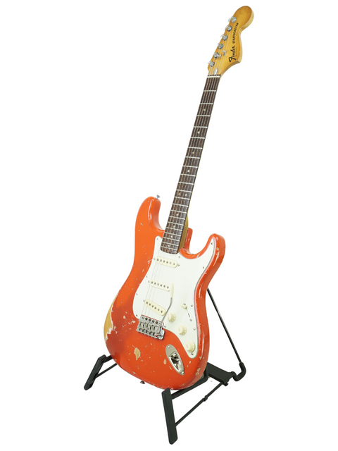 A vibrant red 1979 Fender Stratocaster guitar resting on a stand, highlighted by a simple white background.