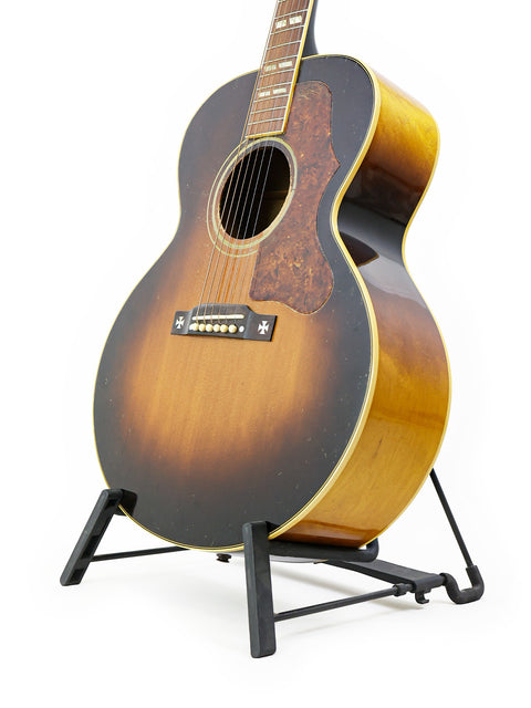 A vintage 1952 Gibson J-185 guitar resting on a stand, with a stark white background that accentuates its timeless appeal.