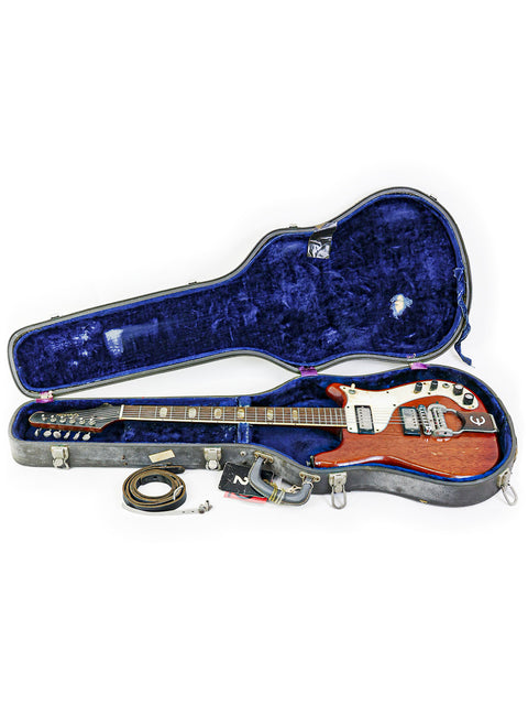 A vintage Epiphone Crestwood Custom guitar is in its case, with another guitar casually resting on the floor next to it.