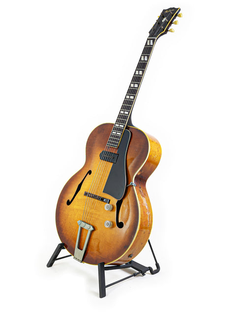 A vintage Gibson ES-300 guitar from 1946 rests on a stand, contrasting beautifully with the white background.
