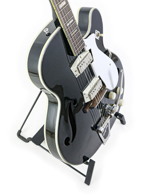 A vintage black guitar on a stand, the Silvertone 1446, displayed against a simple white backdrop for a striking look.