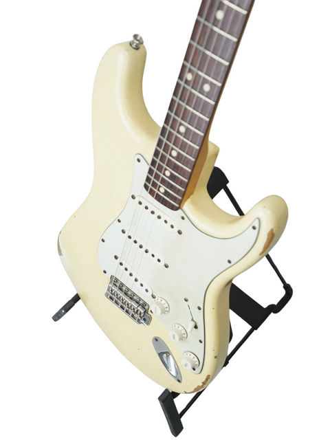 A white electric guitar, specifically a Fender Custom Shop Limited '64 Stratocaster Relic, showcased on a stand.