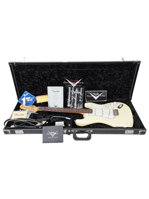 A white guitar case with a Fender Custom Shop Limited '64 Stratocaster Relic and assorted guitar accessories inside.