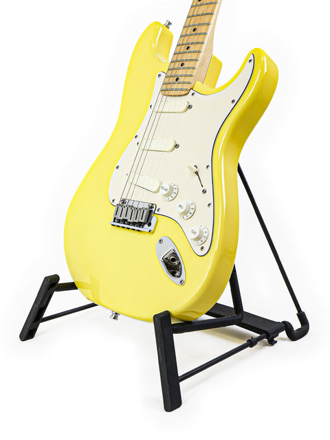 A yellow electric guitar on a black stand with a white background.