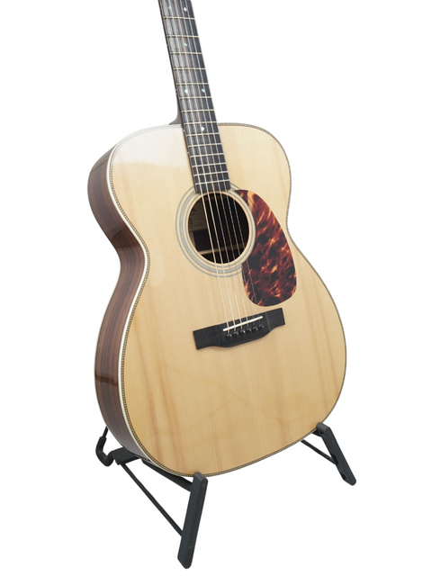 Acoustic guitar on a stand with a light wood finish and a tortoiseshell pickguard.