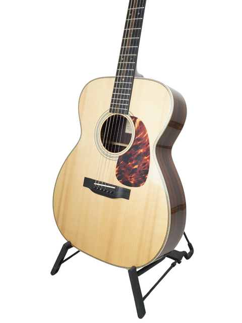 An acoustic guitar displayed on a black stand against a white background.