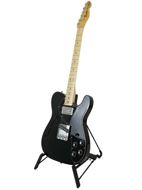 Black electric guitar with a maple neck on a stand against a white background.