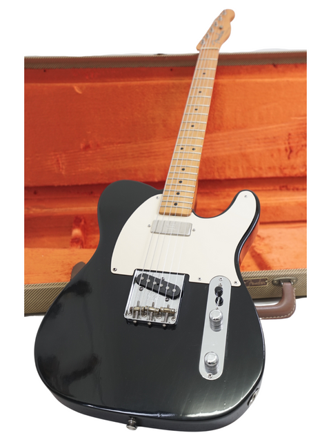 Black electric guitar with white pickguard leaning against a wooden surface.