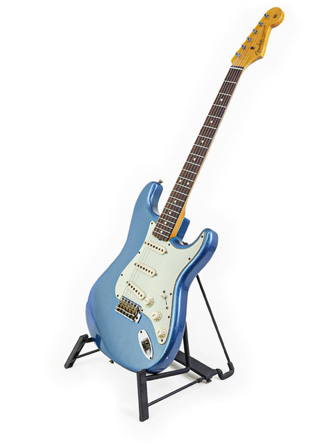 Blue '62 Stratocaster Relic guitar on a stand, showcasing its vintage design against a clean white backdrop.