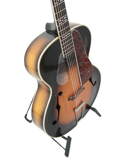 Classic 1937 Old Kraftsman guitar displayed on a stand with a simple white backdrop.