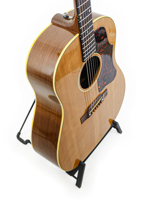 Classic 1956 Gibson J-50 guitar on a stand, highlighted by a simple white background for a timeless look.