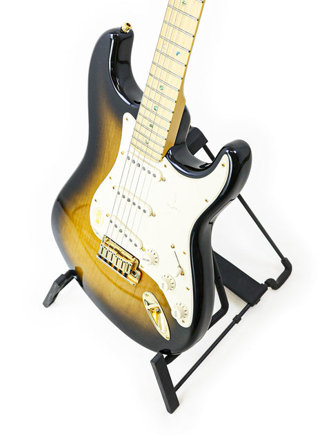 Sunburst electric guitar on a stand against a white background.