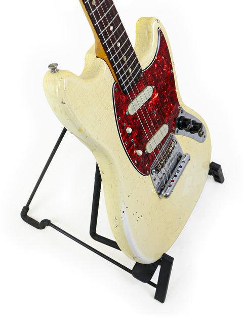 Vintage 1967 Fender Mustang guitar featuring a white body and red neck, resting on a stand, ready to play.