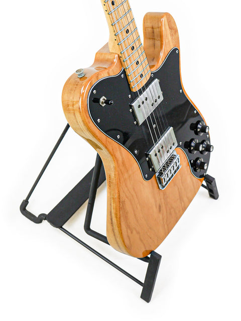 Vintage 1973 Fender Telecaster Deluxe resting on a sleek black stand, showcasing its classic design and craftsmanship.