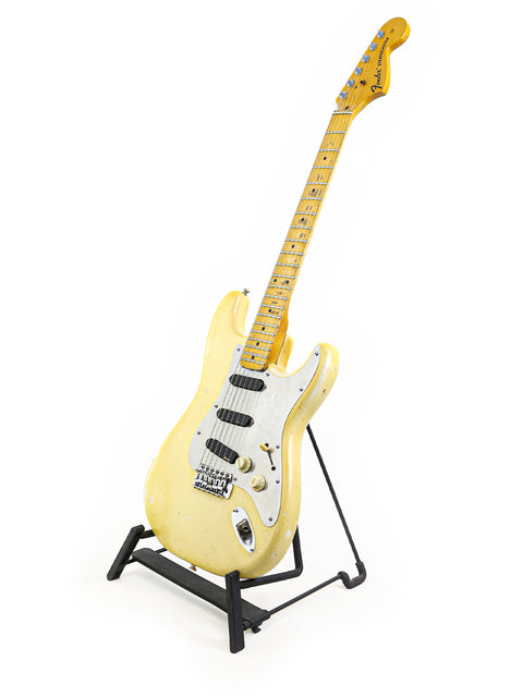 Vintage 1974 Fender Stratocaster in yellow, poised on a stand with a pristine white background, highlighting its classic design.