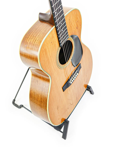 Vintage 1974 Martin 000-28 guitar on a stand, featuring a minimalist white background.