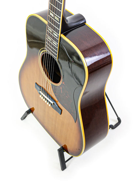 Vintage Gibson Southern Jumbo guitar on a stand against a clean white background, showcasing its classic design from 1964.