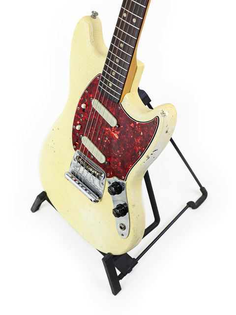 White 1967 Fender Mustang guitar featuring a red pickguard, beautifully positioned on a stand, perfect for any music lover.