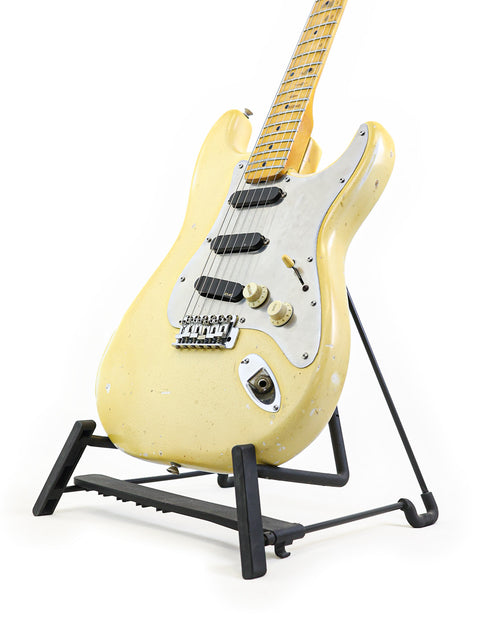 White 1974 Fender Stratocaster guitar resting on a stand with a black base, showcasing its vintage charm.