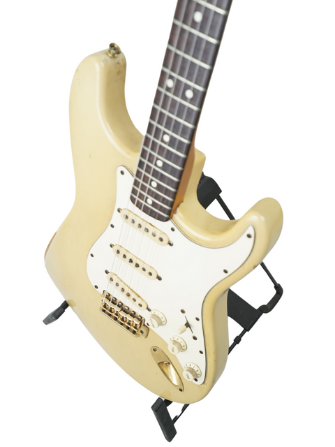 White electric guitar, Fender Custom Shop '59 Stratocaster Reissue, displayed on a black stand, highlighting its vintage appeal.