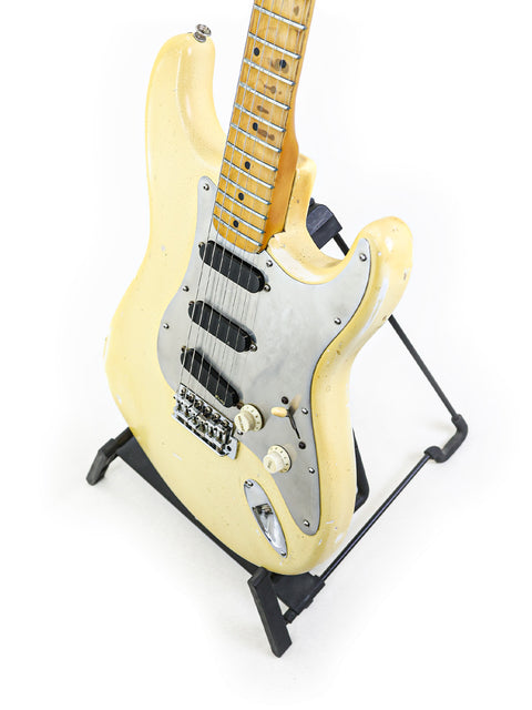 White electric guitar on a stand, a vintage 1974 Fender Stratocaster with a striking black pick guard.