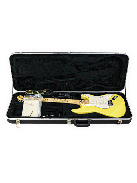 Yellow electric guitar in black case with accessories.