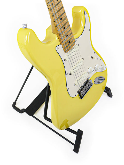 Yellow electric guitar on a stand against a white background.