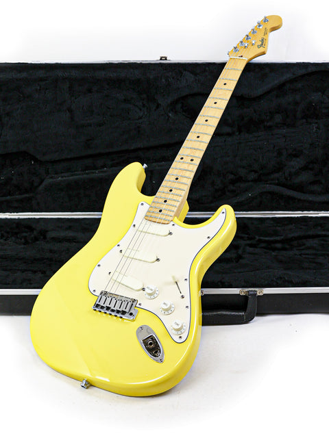 Yellow electric guitar with a maple fretboard against a black case background.