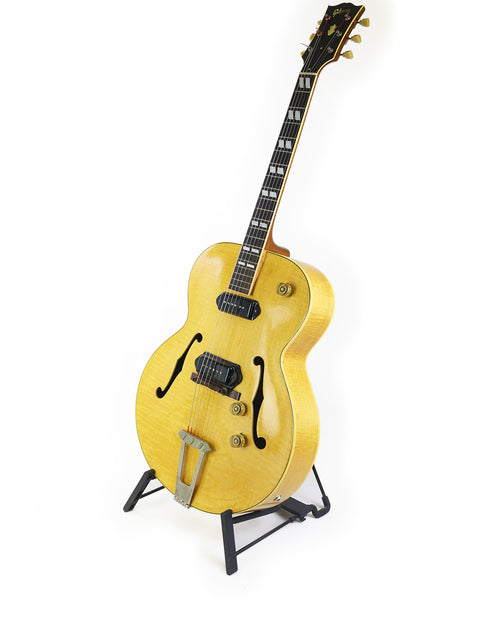 1952 yellow Gibson ES-300 guitar showcased on a stand with a plain white background.